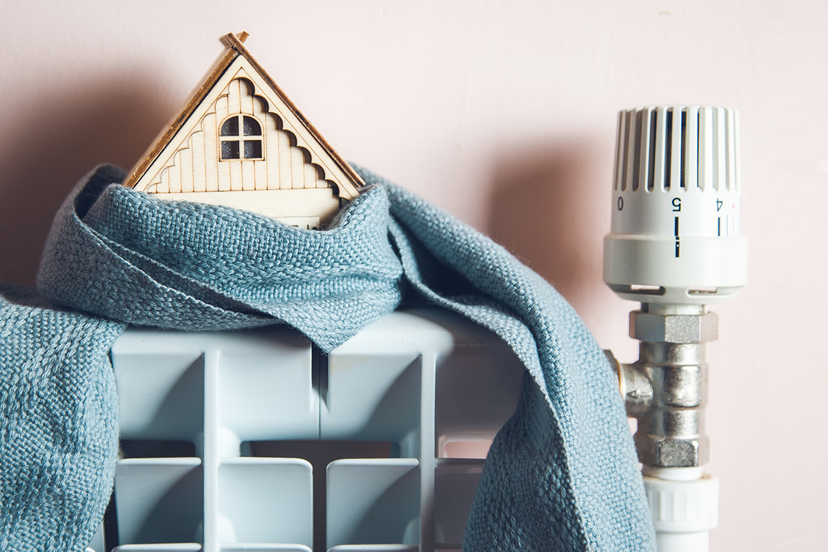 A radiator with a little wooden house sitting on top, wrapped in a blue scarf